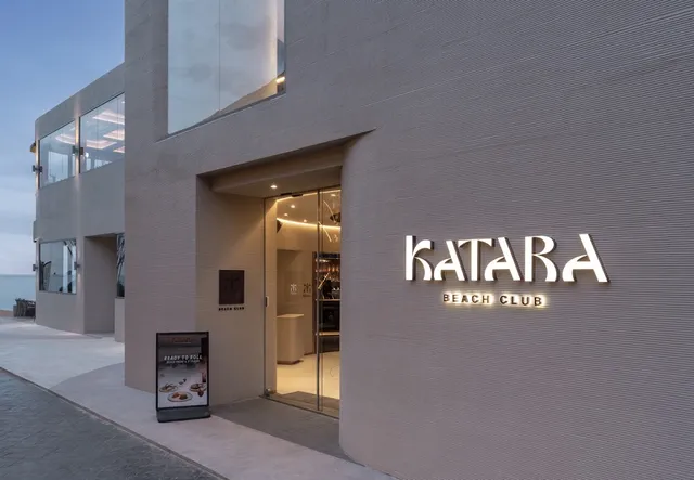 A modern gray stone facade with a glass entrance and an illuminated sign