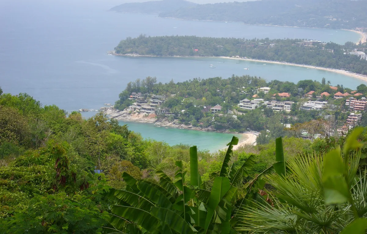 An elevated view over three bays with pale sand and turquoise water, tropical plants in the foreground