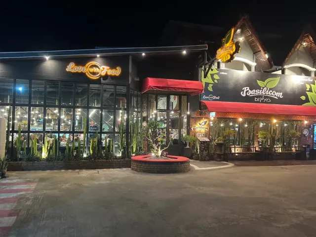 A restaurant complex front at night with neon signs, a cactus bed and a round planter