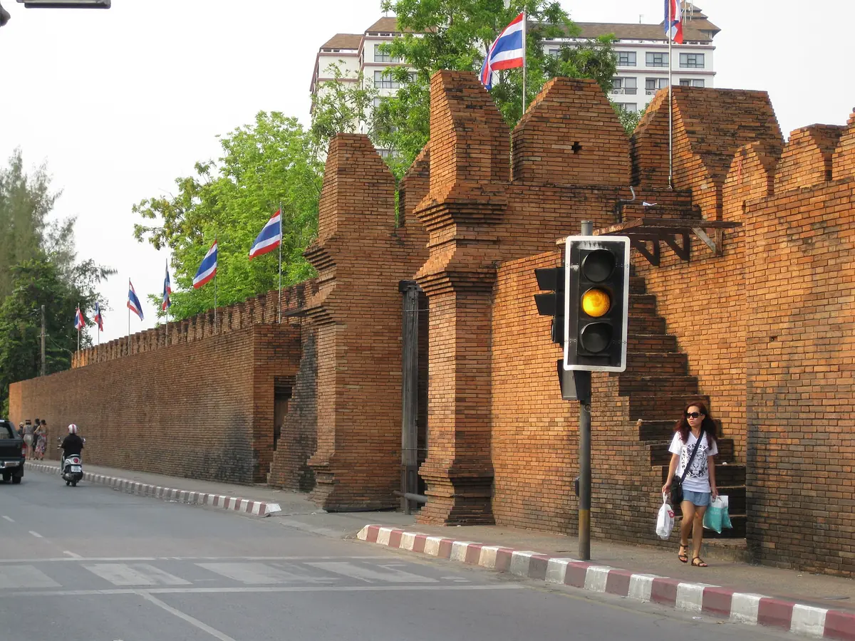 An ancient brick wall with crenellated bastions and flags, along a city road in warm afternoon light