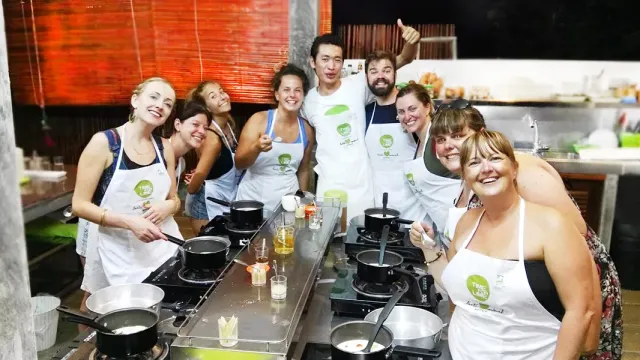 A group of participants in white aprons posing beside cooking stations with pans