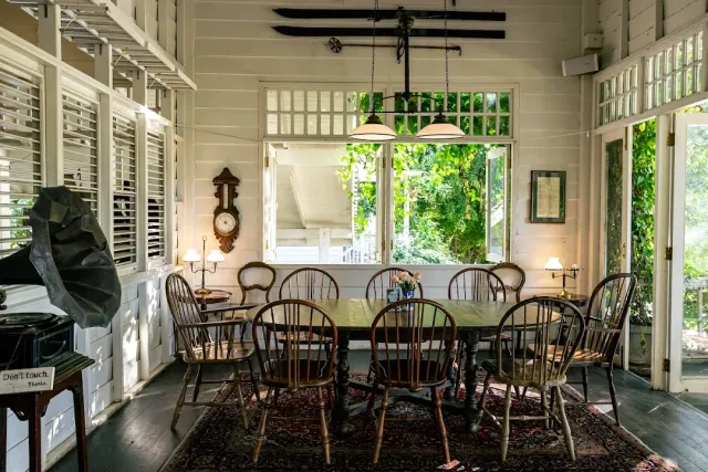 A white colonial style dining room with a wooden table and chairs facing a window open to the garden