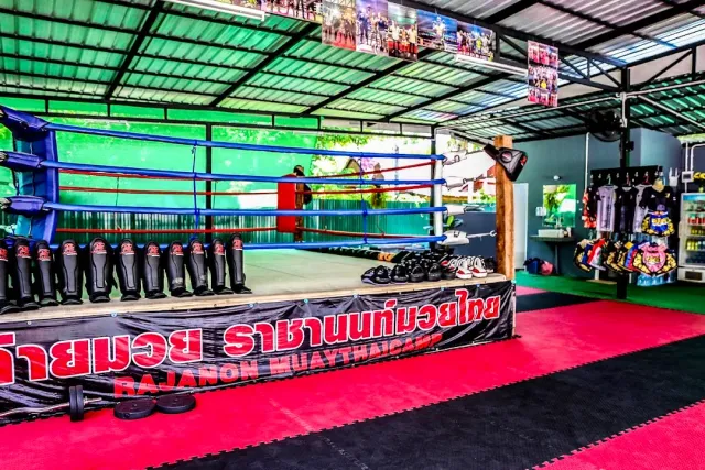 A ring with blue ropes, shin guards lined up in a row and red mats