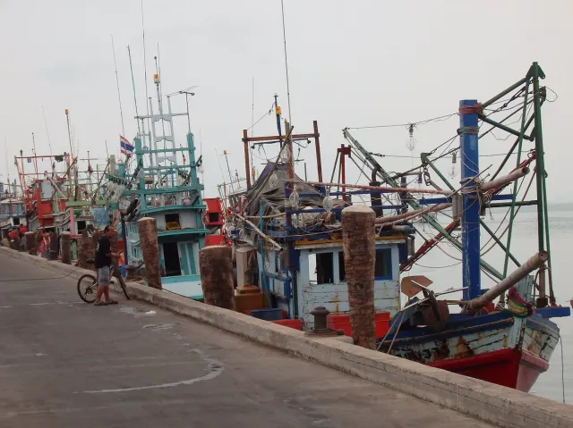 A row of colorful fishing boats moored along a concrete quay on a cloudy day