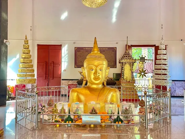 The upper body of a gilded Buddha surrounded by a metal railing and flower offerings