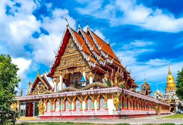 An ornate temple hall with tiered roofs and a gilded chedi beside it, blue sky