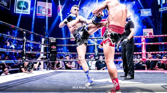 Two fighters in a lit ring, one landing a high kick in front of a crowd