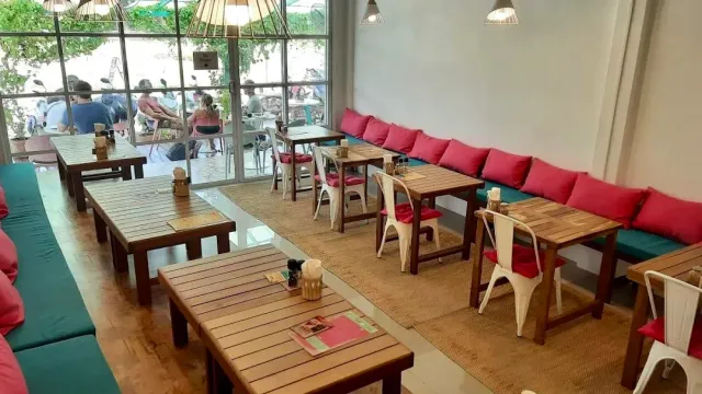Wooden tables facing a bench with pink cushions, and a front open to the street