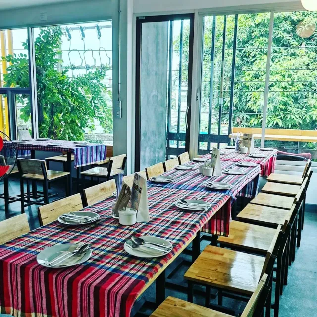 Long tables with red checked cloths, set dishes and windows onto greenery