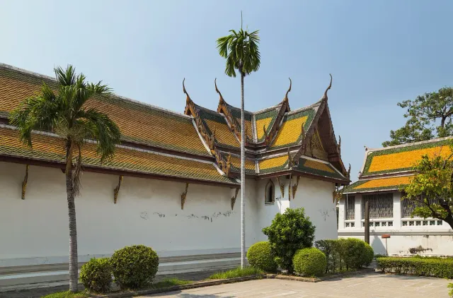 A temple hall with a tiered tile roof and gilded trim among palms and tended gardens