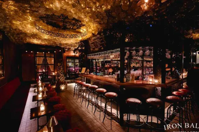 A curved bar in dim light, a glittering golden ceiling and red leather stools