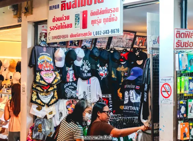 A clothing stall with shirts and caps hanging, two shoppers choosing from the rack