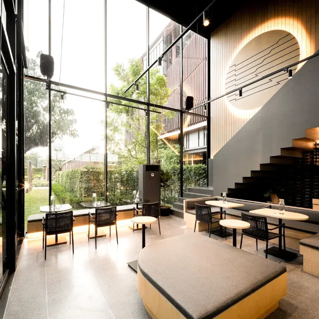 A modern space with a glass wall to the garden, wooden stairs and round tables