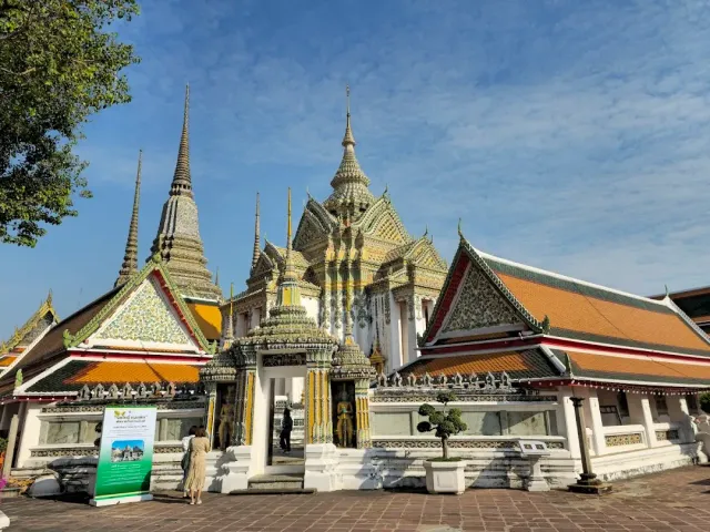 A temple courtyard with decorated chedis, a gilded gate and orange tiled roofs