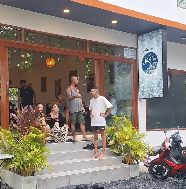Visitors chatting on the entrance steps, a lit sign and plants on both sides of the doorway