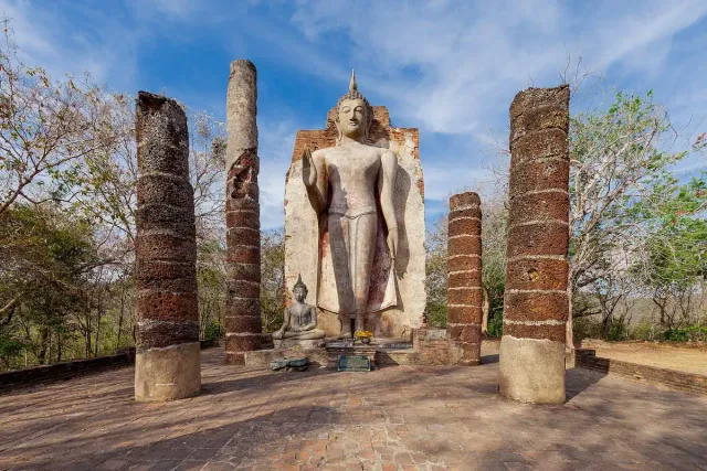 A standing stone Buddha figure between two tall brick columns on a hilltop