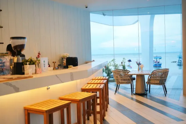 A white marble counter with wooden stools and a glass wall onto the sea and anchored boats