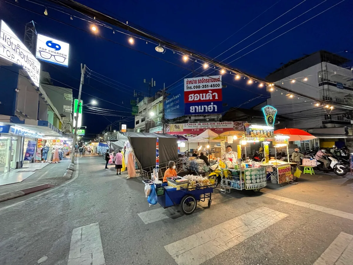An evening market street with strings of bulbs, mobile food carts and lit signs