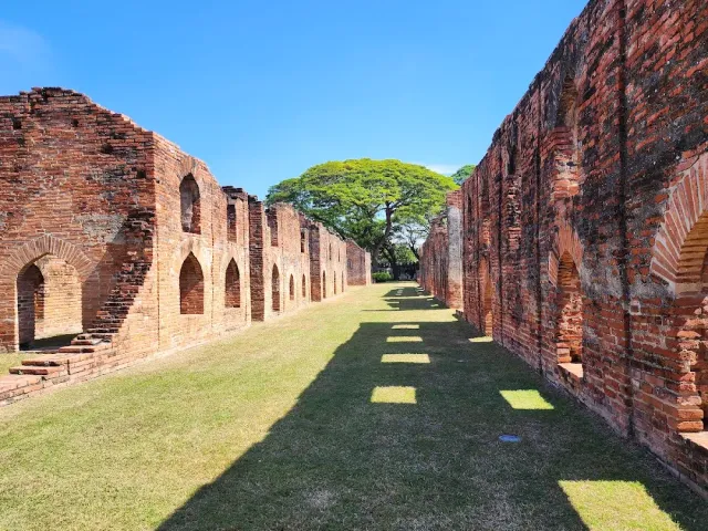 Two long brick walls with arched niches, a lawn and a tree in the middle