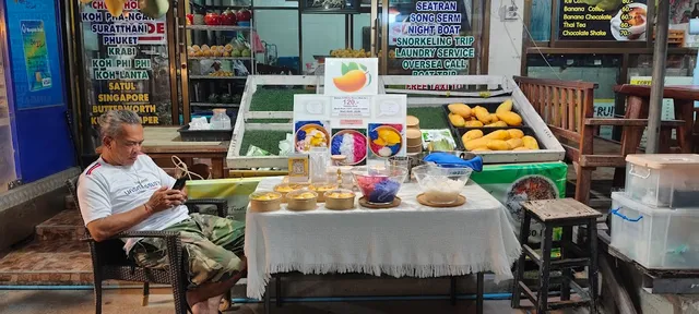 A dessert stall with yellow mangoes and boxes of sticky rice on a white table