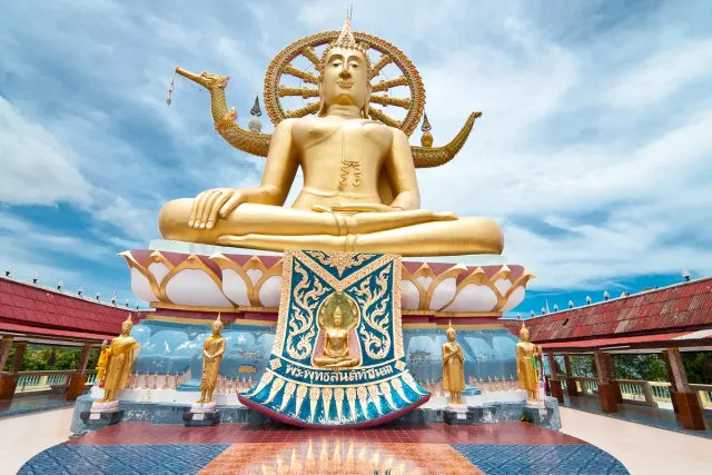 A giant gilded seated Buddha figure on a lotus base under a blue sky