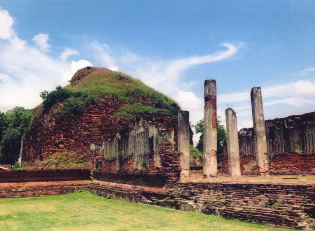 A grass covered mound of brick ruins with three standing stone columns beside it