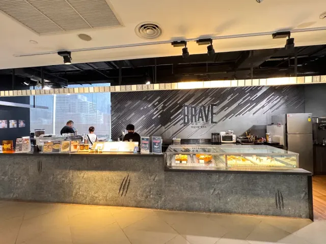 A long coffee bar counter with a pastry display, against a grey wall with a sign