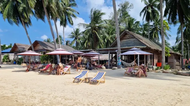 Deck chairs and parasols on white sand facing wooden huts among palms