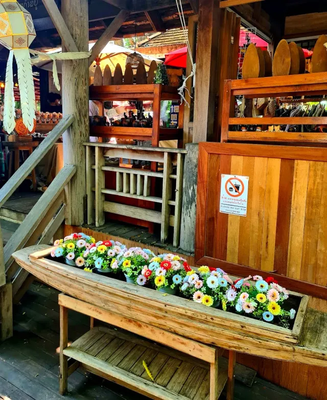 A rustic wooden building with a long boat full of colorful flower pots in front