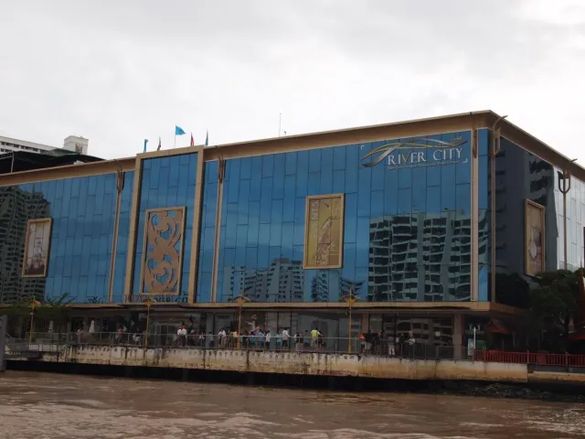 A modern commercial building with a dark glass frontage beside skyscrapers and a river