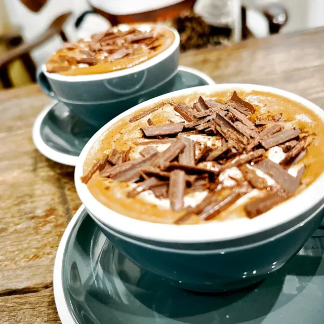 Two blue cups with coffee foam and chocolate shavings, on a wooden table