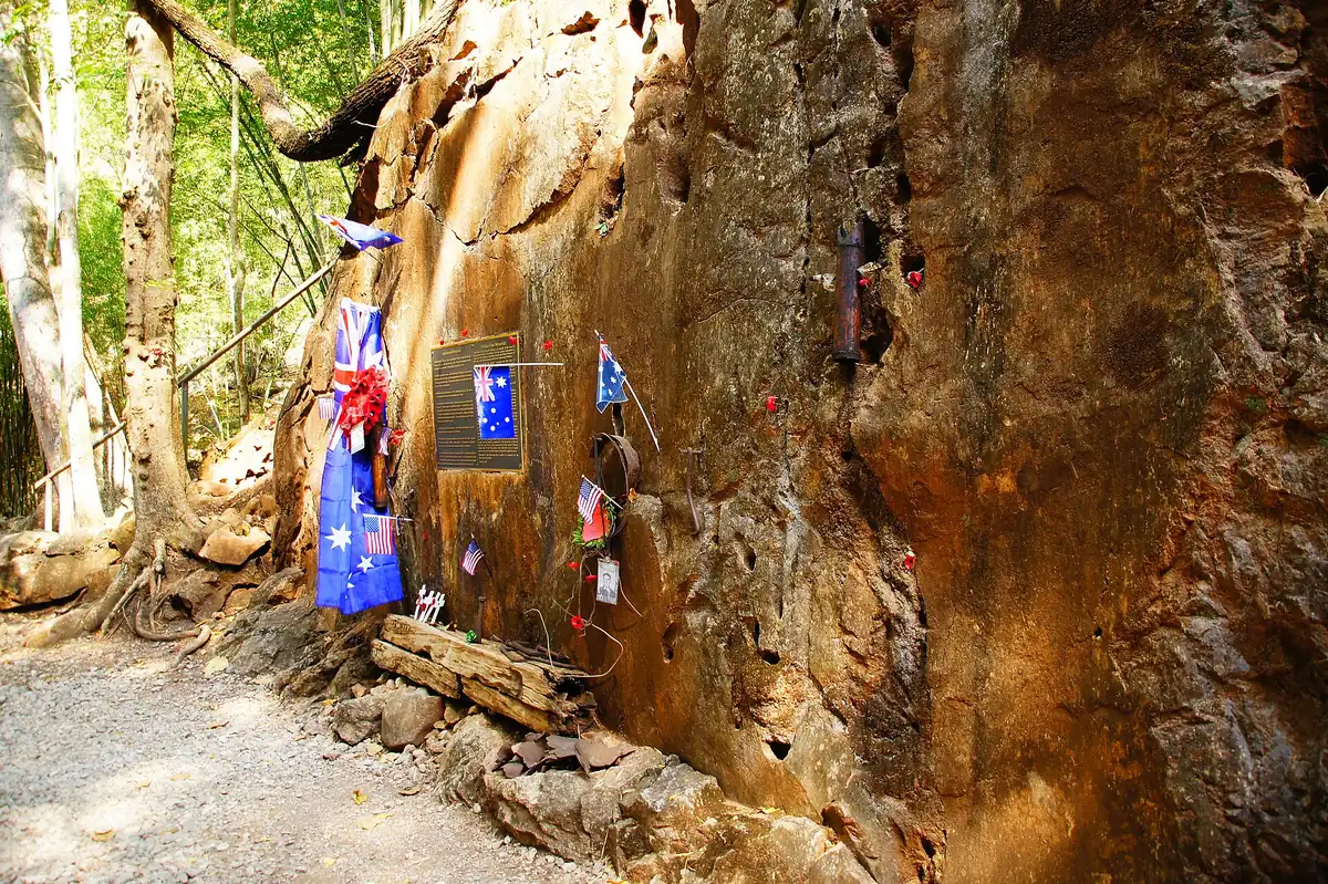 Cut rock wall along a trail with memorial plaques and small flags fixed to it