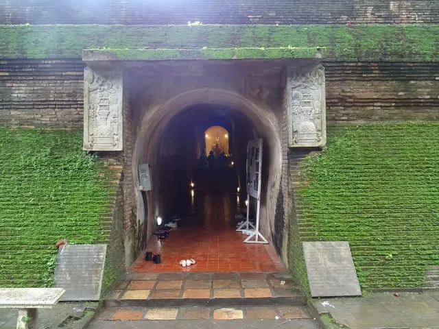 The arched brick entrance of a tunnel in a moss covered wall, with a lit figure deep inside