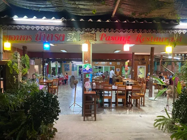 An open space at night with a lit colorful sign, colored lamps and wooden tables