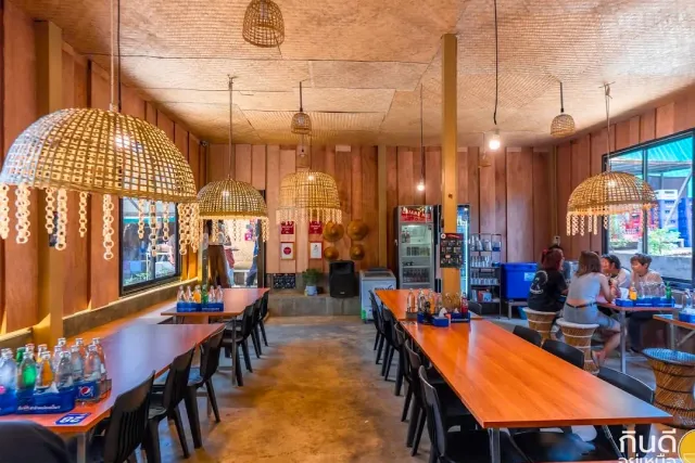 A hall with wooden walls, long orange tables and hanging rattan lights