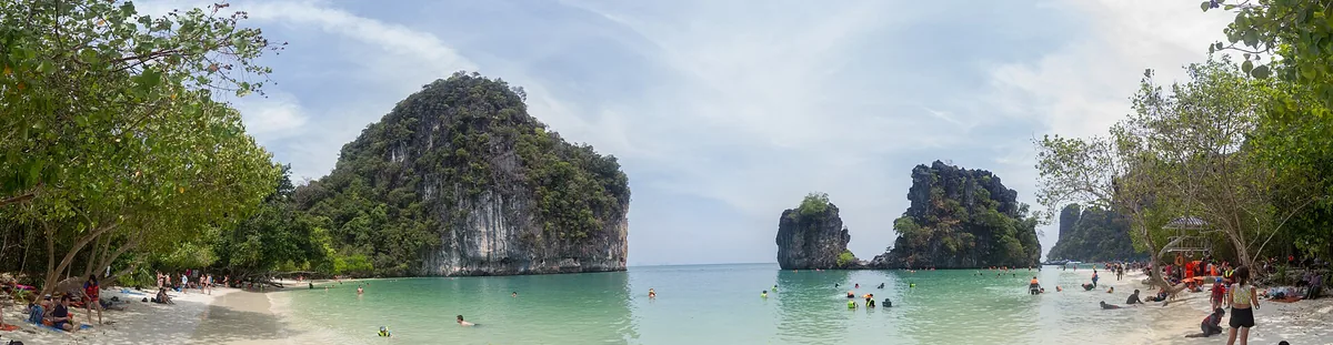 Forested limestone cliffs on both sides of shallow green water with bathers