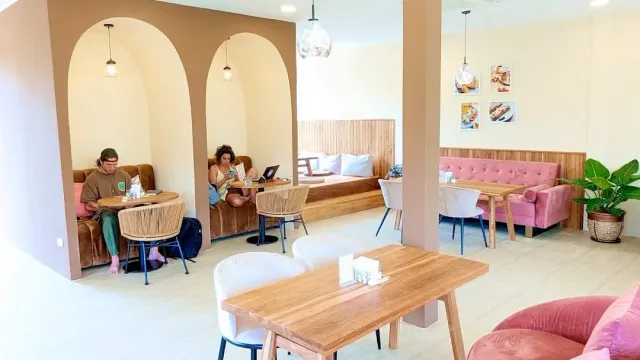 A pastel toned space with arched alcoves, a pink sofa and light wooden tables