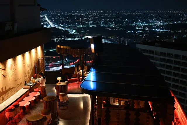 A lit bar counter on a building roof with a night sky and city lights behind