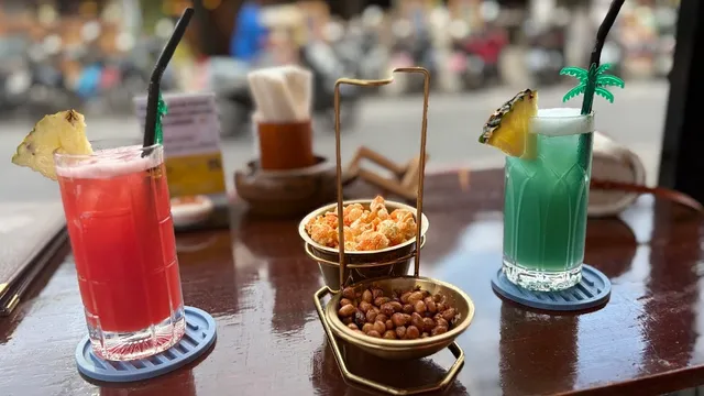 Two colorful cocktails with pineapple on a table, next to small bowls of snacks