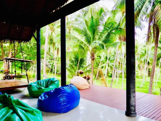 An open pavilion with colorful beanbags and a wooden floor, a coconut grove beyond the pillars