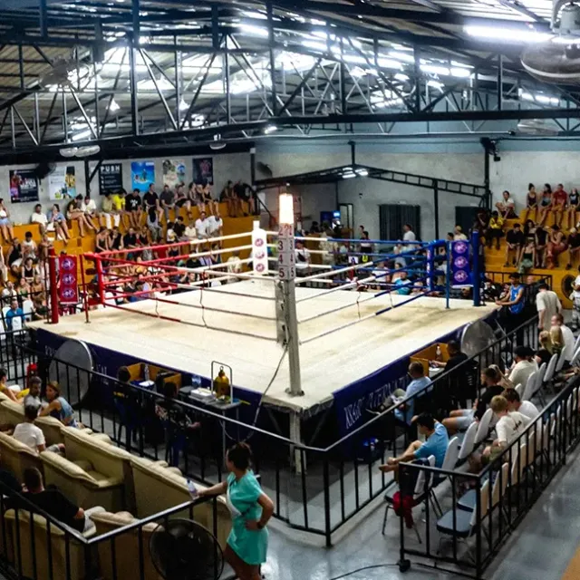 An empty boxing ring in a covered hall with stands full of spectators around it