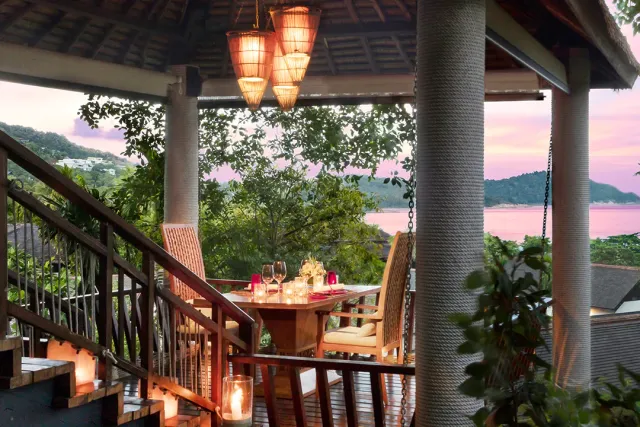 An elevated wooden terrace with a candlelit set table and pink skies over the bay