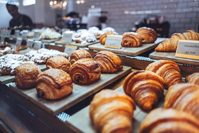 Rows of croissants and chocolate pastries on wooden trays in a display