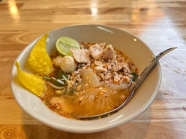 A bowl of spicy noodle soup with meatballs, minced meat and lime