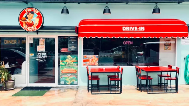 A pale blue diner front with a red awning and red tables outside