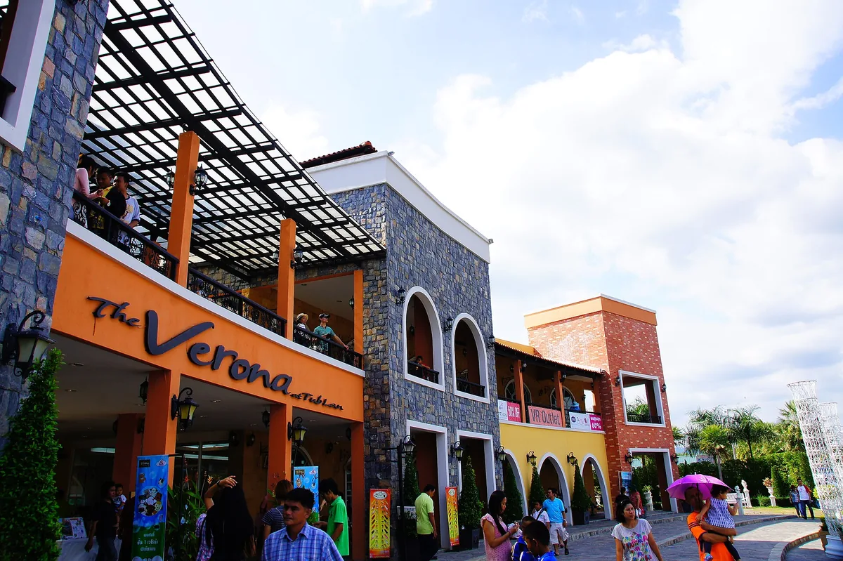 Italian styled retail complex in orange and yellow with arches and visitors under a blue sky