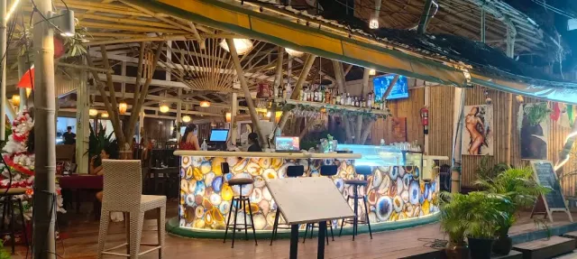 A bamboo roofed drinks counter with a colorful stone front and tall stools