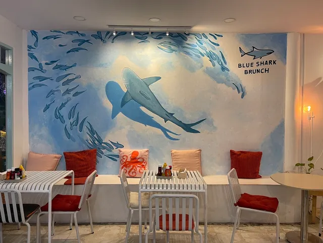 A mural of a shark and a school of fish above a bench with colorful cushions