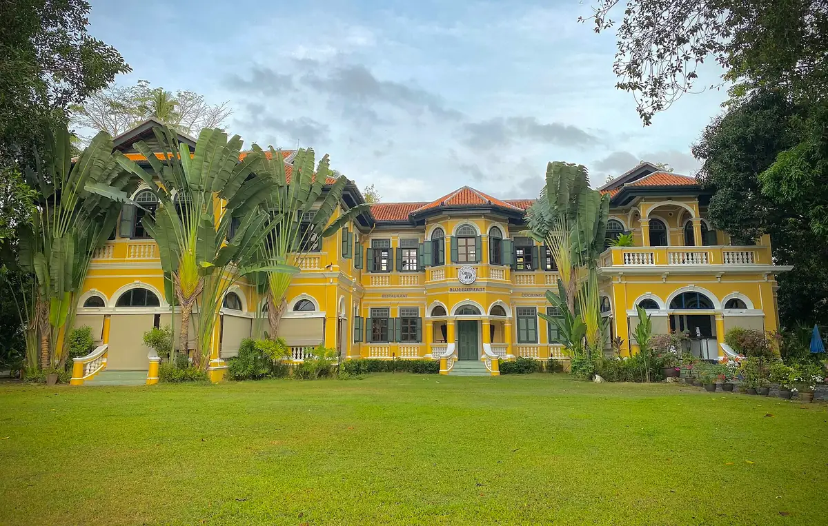 A yellow colonial mansion with dark shutters and arches, on a wide green lawn