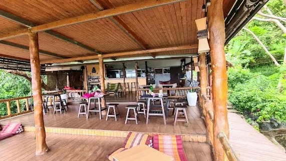 A covered wooden terrace with high stools and a view of tropical greenery